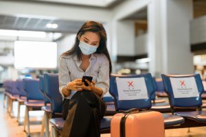 Young,Asian,Tourist,Woman,With,Mask,Using,Phone,And,Sitting